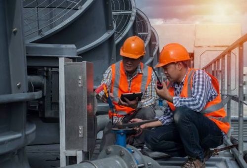 Two Asian engineer discuss job with  tablet  on cooling tower background. Two worker co-worker on cooling tower.