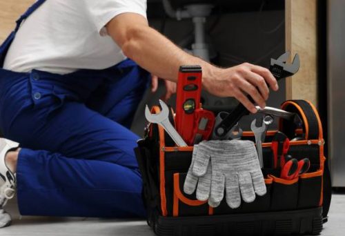 Professional plumber taking adjustable wrench from tool bag indoors, closeup