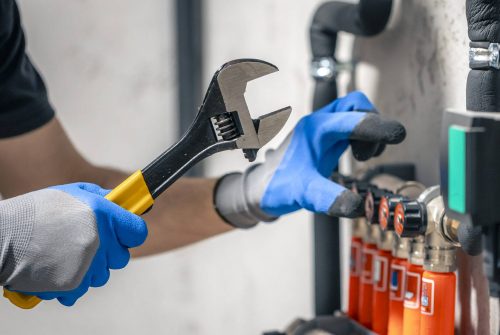 A man installs a heating system in a house and checks the pipes with a wrench. Adjusting heating valves in a residential building. A plumbing and heating technician works.