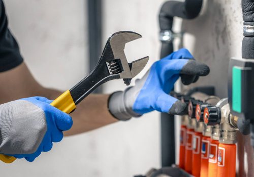 A man installs a heating system in a house and checks the pipes with a wrench. Adjusting heating valves in a residential building. A plumbing and heating technician works.