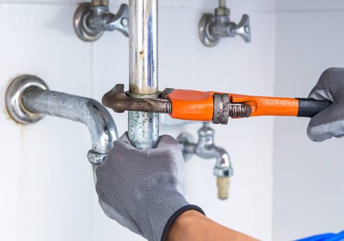 Technician plumber using a wrench to repair a water pipe under the sink